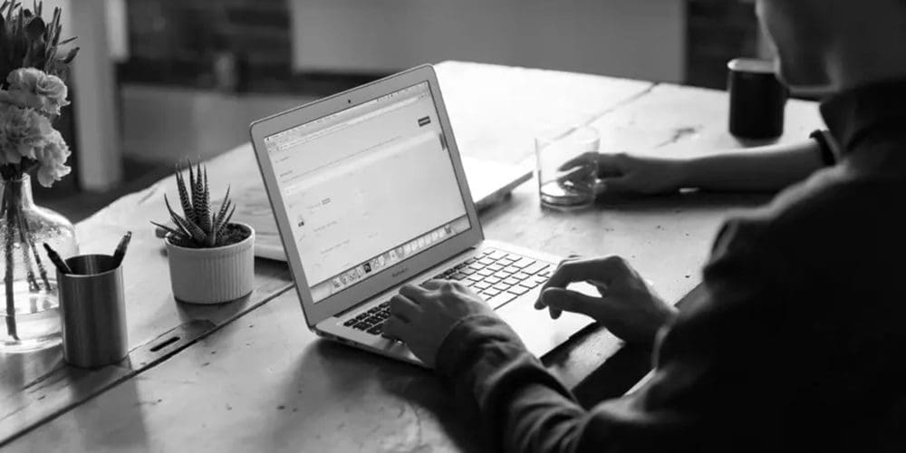 A man is sitting at a desk typing on his work computer.