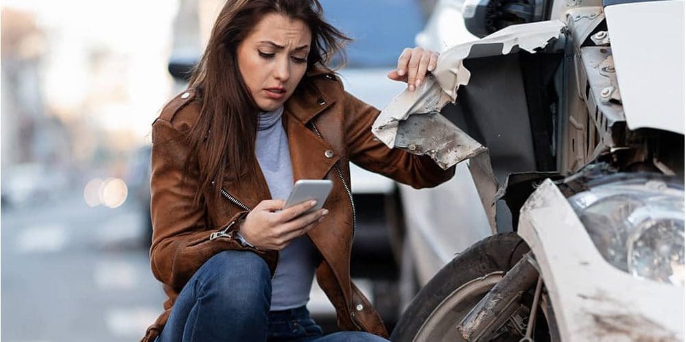 A woman is making a phone call next to her wrecked car, after getting into an auto accident.