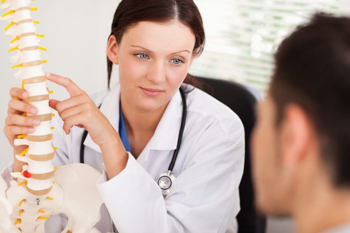 A chiropractor points to vertebrae on a model spine to explain chiropractic manipulation treatments to a new patient.