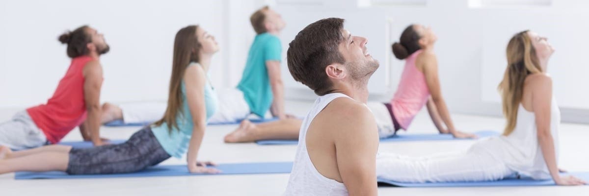 Six people warm up by stretching on yoga matts.