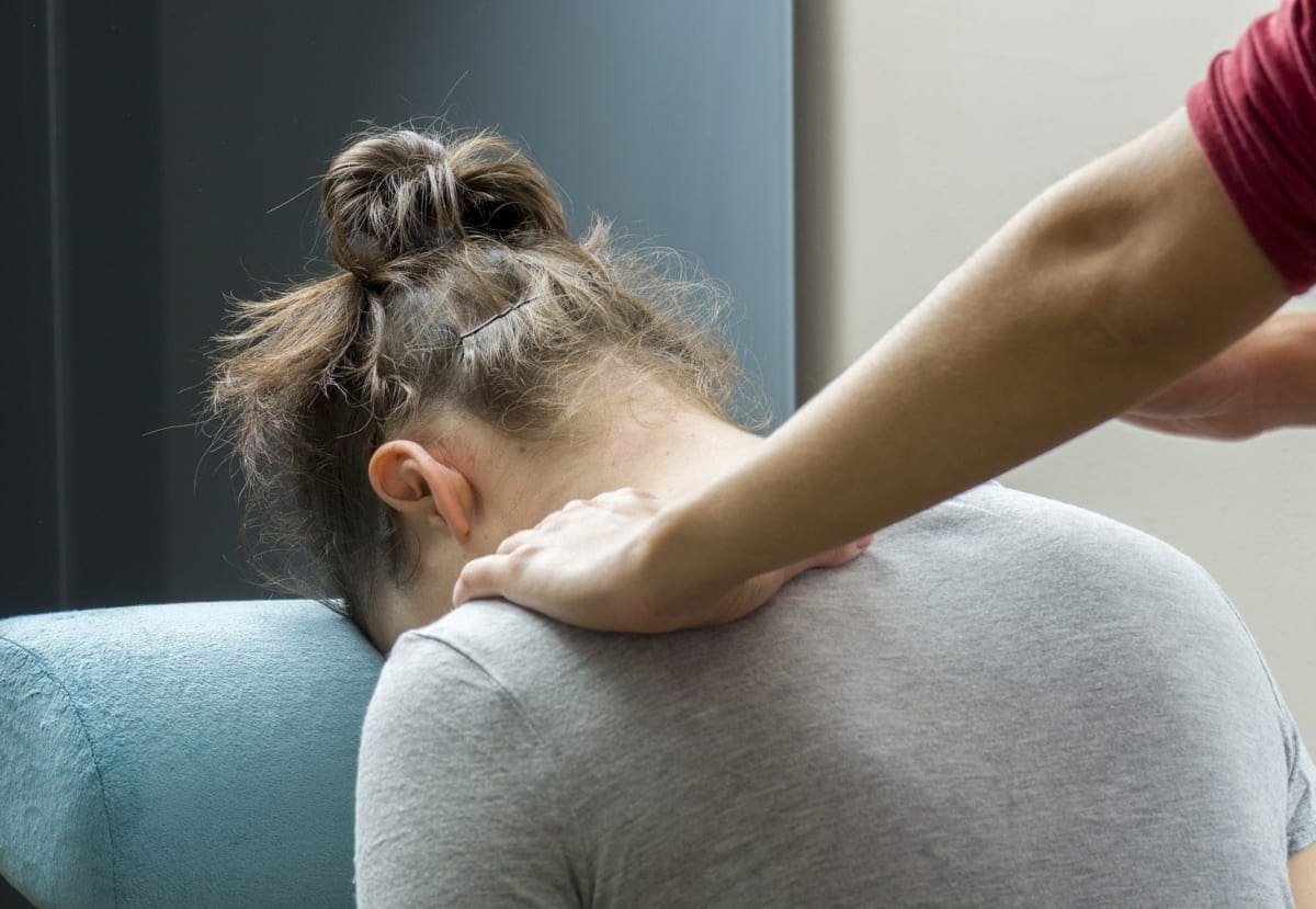 A woman is being treated by a chiropractor for hypertension in the upper back and shoulders.
