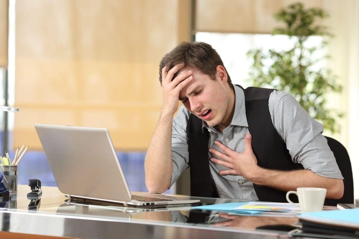 A man is having an anxiety attack while sitting at his work desk.