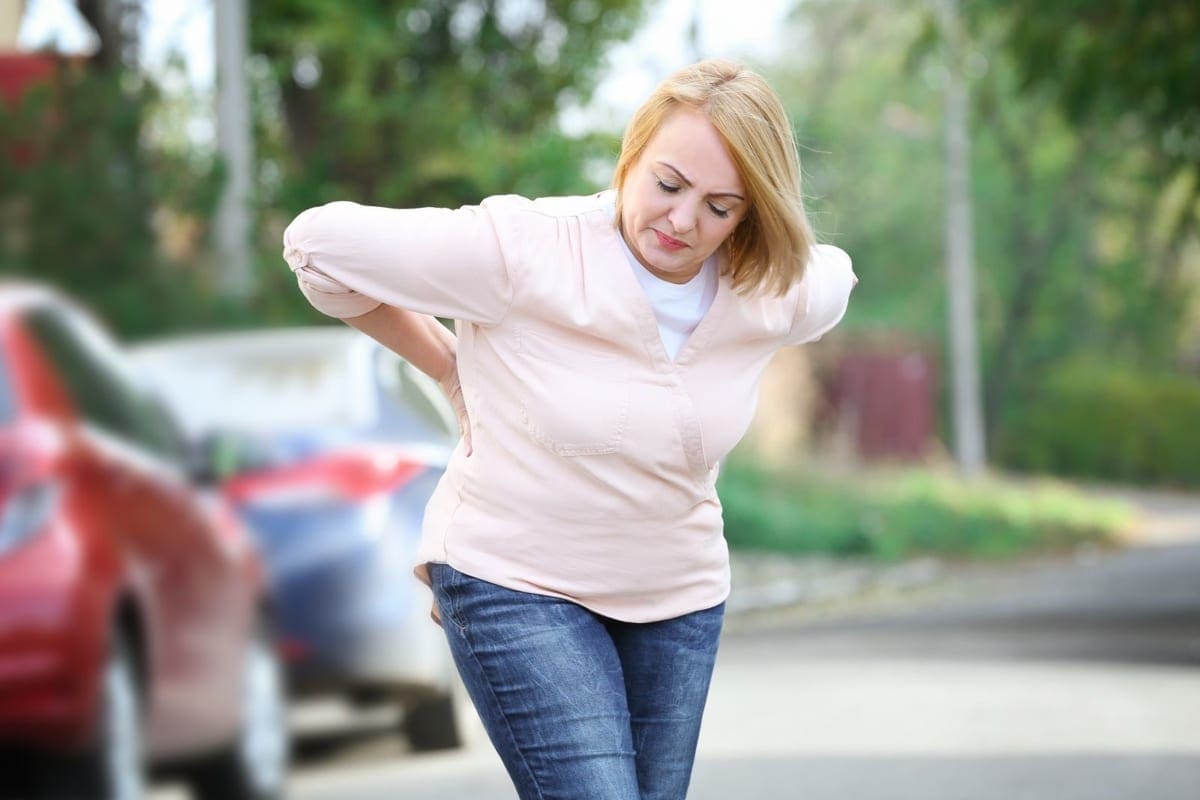 A woman bends forward and struggles because of back pain.