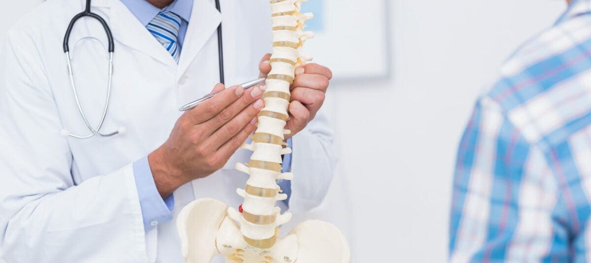 A doctor manipulates the spine of a medical skeleton to demonstrate.