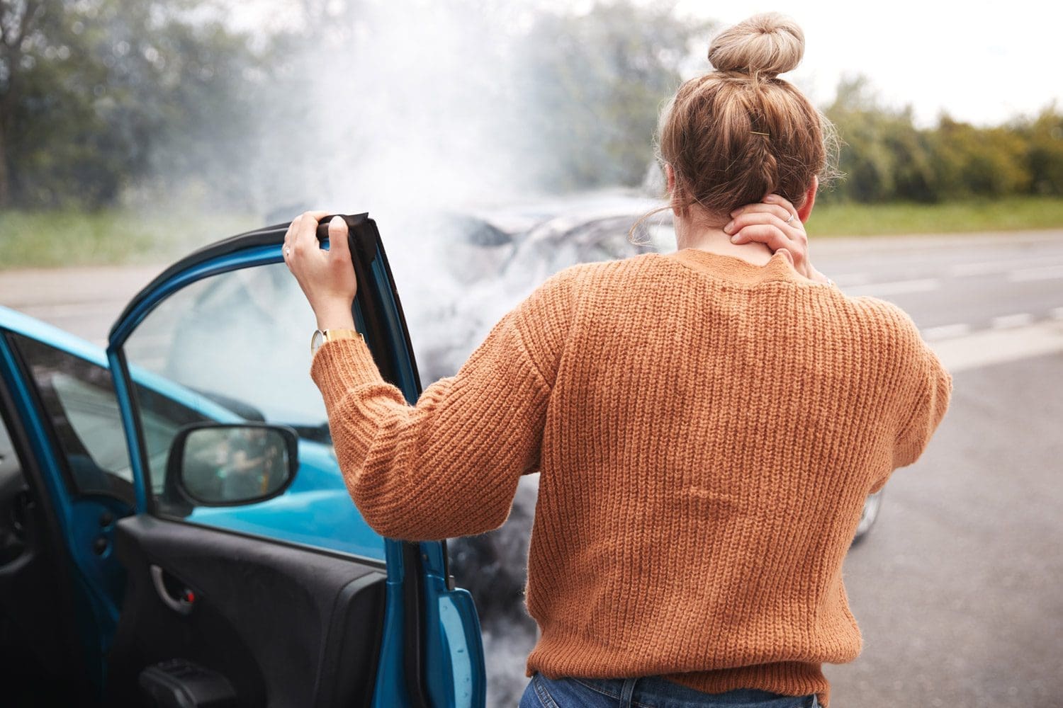 A woman gets out of a wrecked car and holds the back of her neck because it was injured in a car crash.