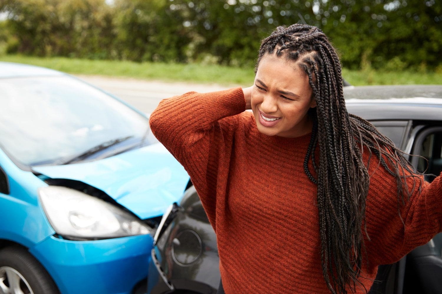A woman winces in pain while getting out of her wrecked car after an accident.