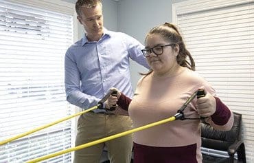 A woman participating in physical therapy exercises with rubber bands under the guidance of a chiropractor.