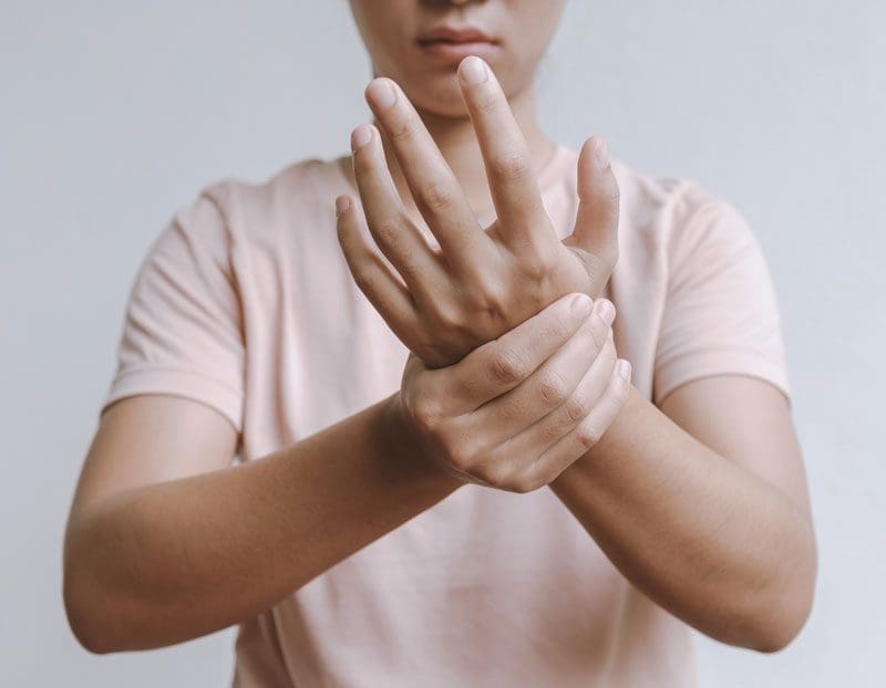 A woman grasps her wrist because she is experiencing tingling in her hand and wrist.