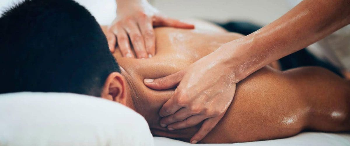 A man laying face down on a massage table receiving a massage from a chiropractic massage therapist.