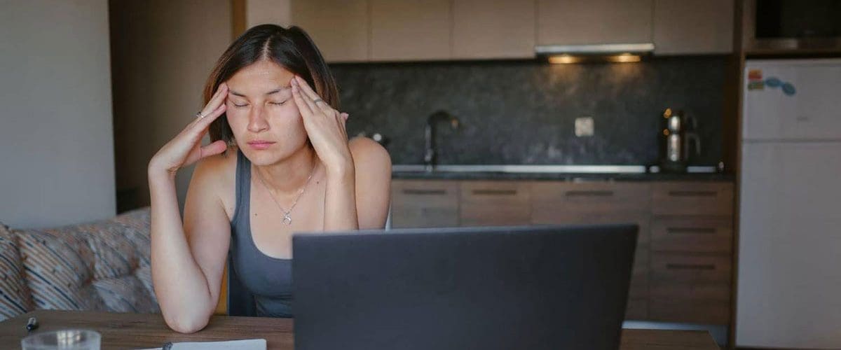 A woman leaning on a table, and squinting from exhaustion and brain fog.