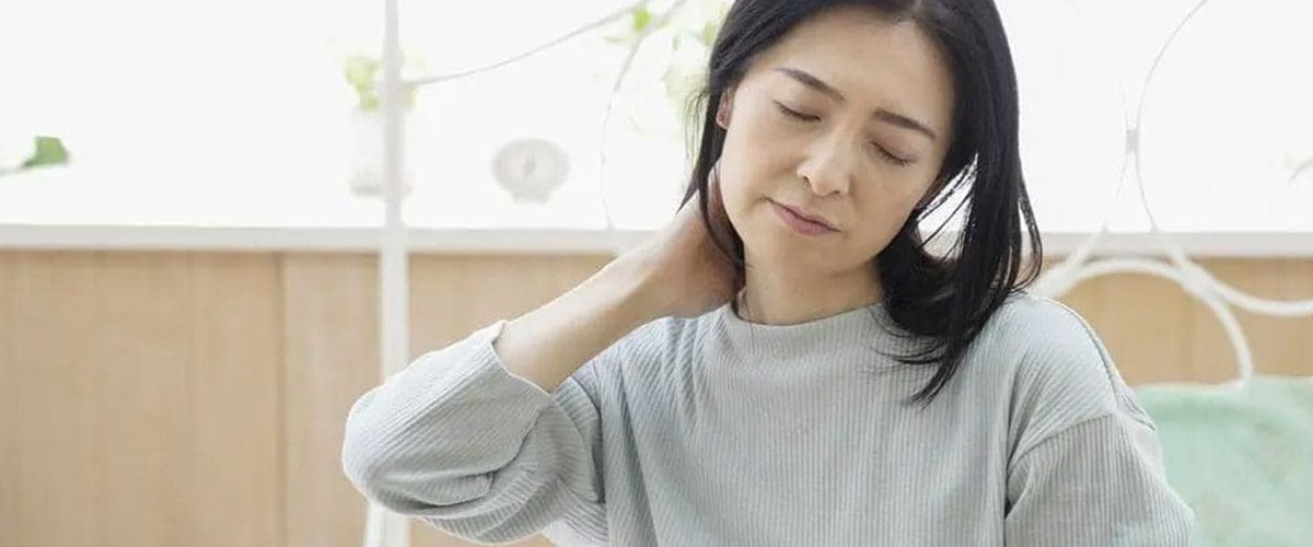 A woman winces and holds her lower neck because of neck pain.