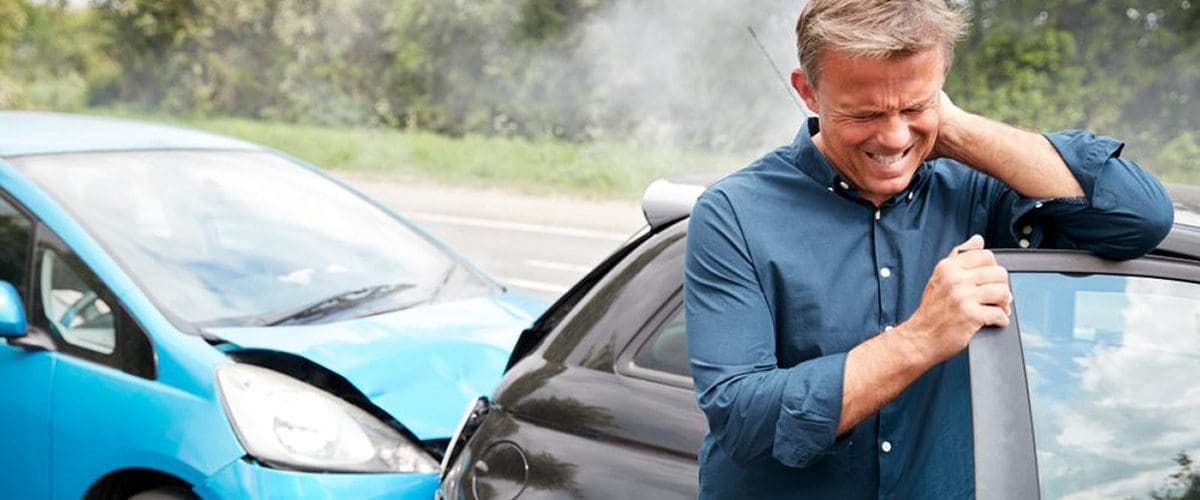 A man is wincing in pain from a whiplash injury after a car accident