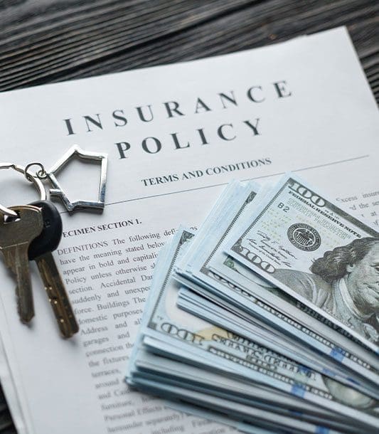 A car accident settlement document sits on a table with car keys and hundred dollar bills on top.
