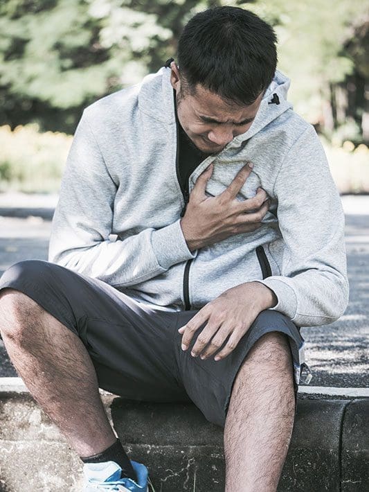 A man is sitting down and grasping his chest because of chest pain.