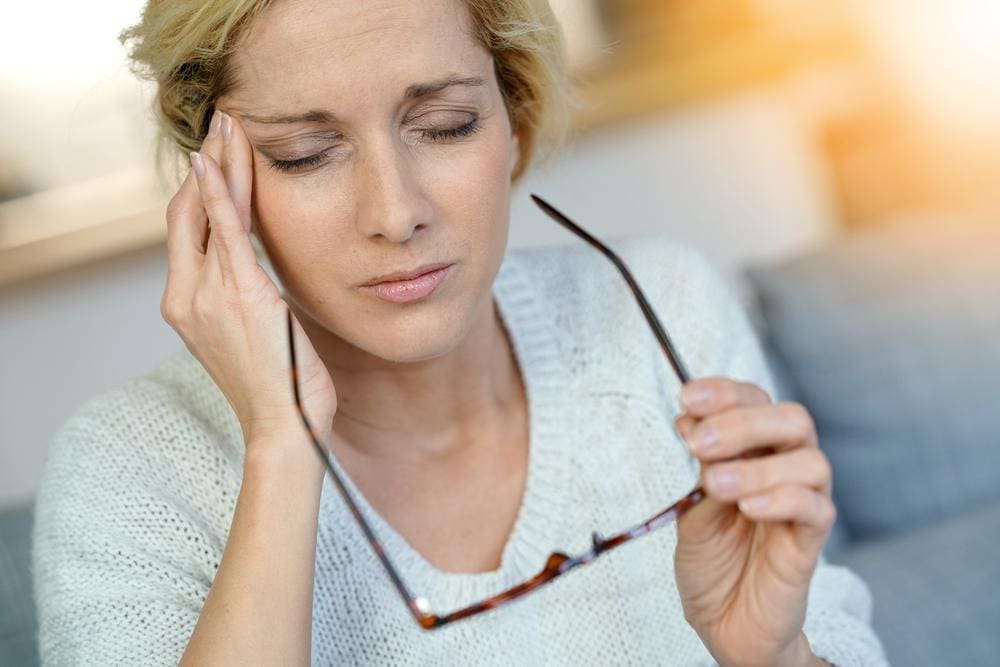 A woman rubs her temple because she is suffering from a migraine headache.