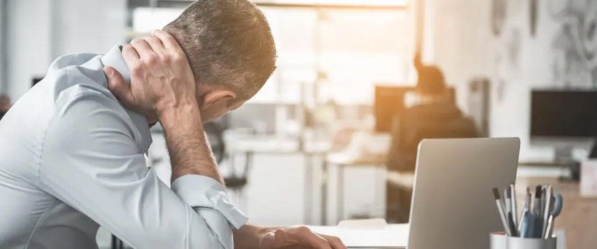 A man sitting at his desk suffering from neck pain