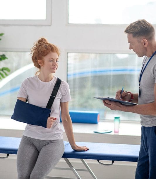 A woman with her arm in a sling is discussing chiropractic care and physical therapy to treat her post auto accident injuries.