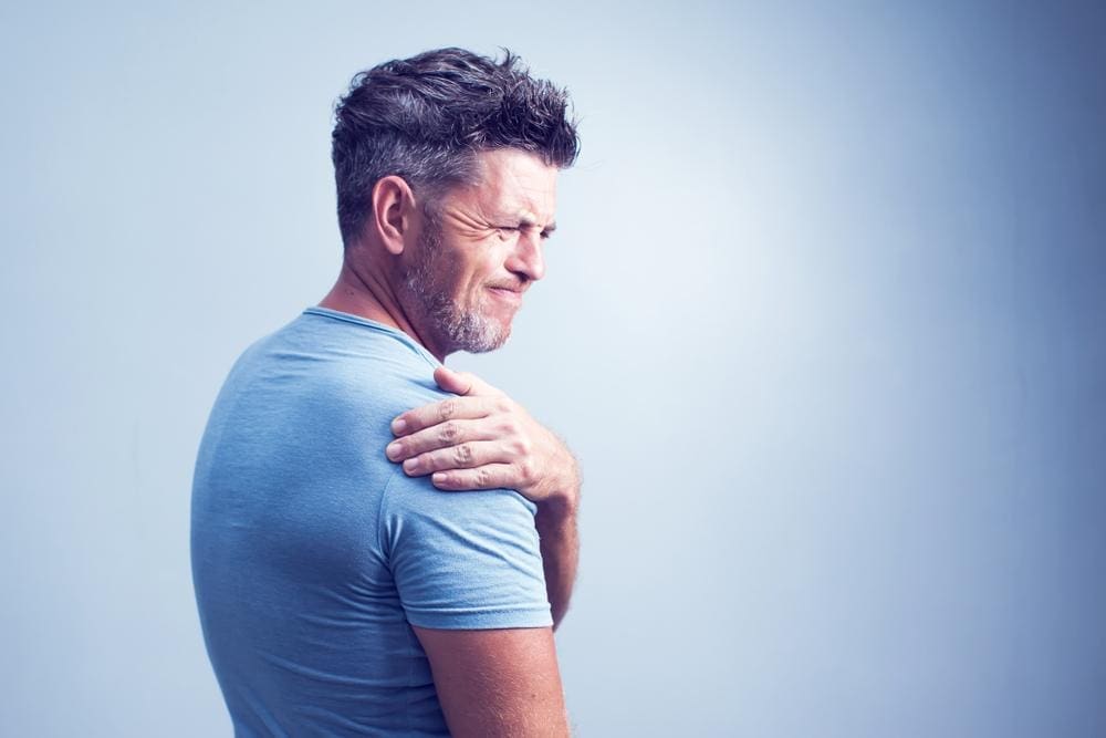 A man winces in pain and is holding his shoulder because of pain from a broken collar bone. 