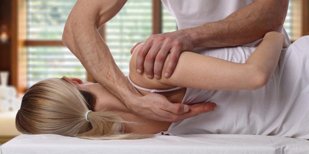 A chiropractor is treating a woman's shoulder blade pain.