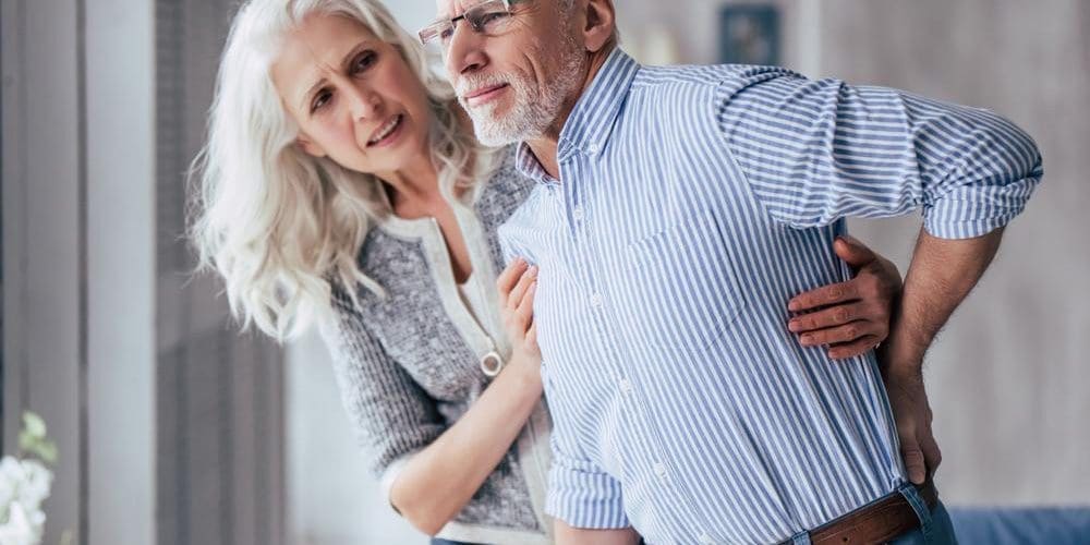A man is struggling to stand upright because of pain from a compression fracture.