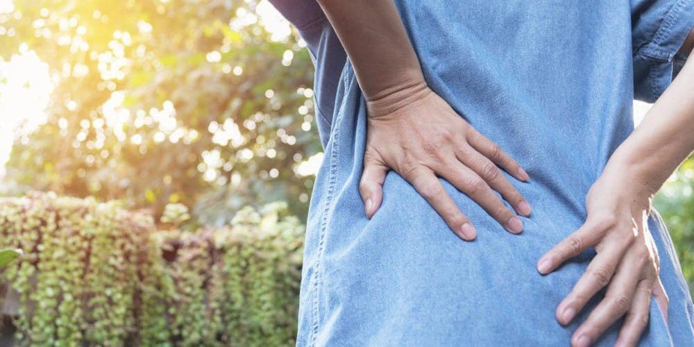 A woman leans forward slightly while holding her lower back because of lower back pain.