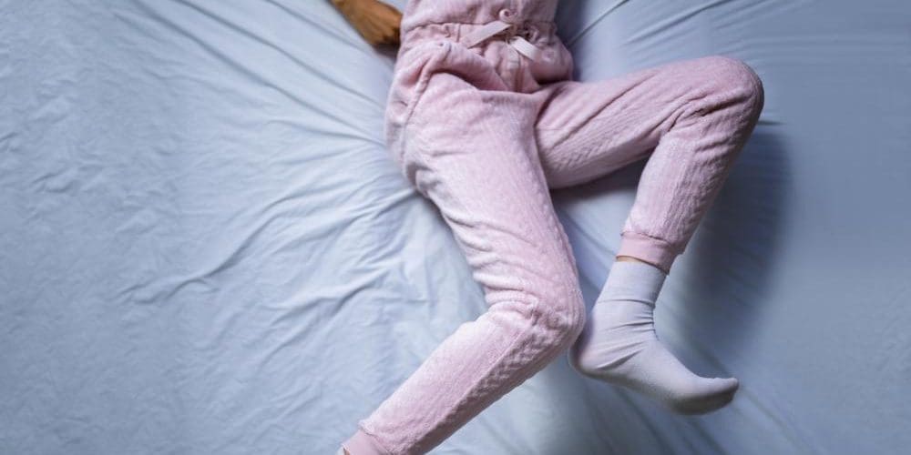 A woman is in bed, trying to sleep, but she can't can't sleep because of restless leg syndrome.