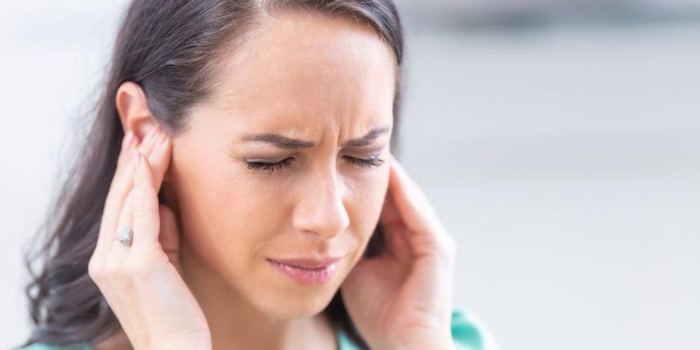 A woman is covering her ears and wincing, because she cannot get the ringing in her ears to stop.