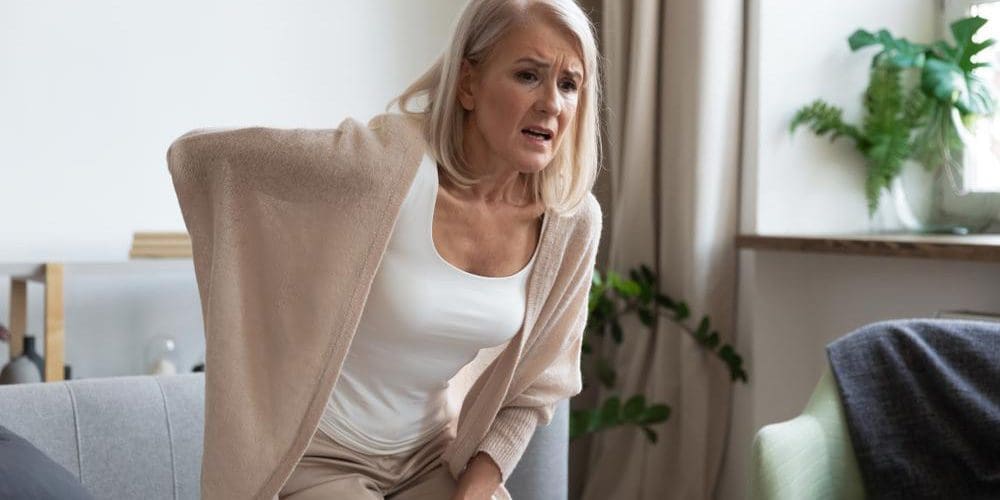 A woman is having a hard time standing up straight because of sciatic nerve pain.