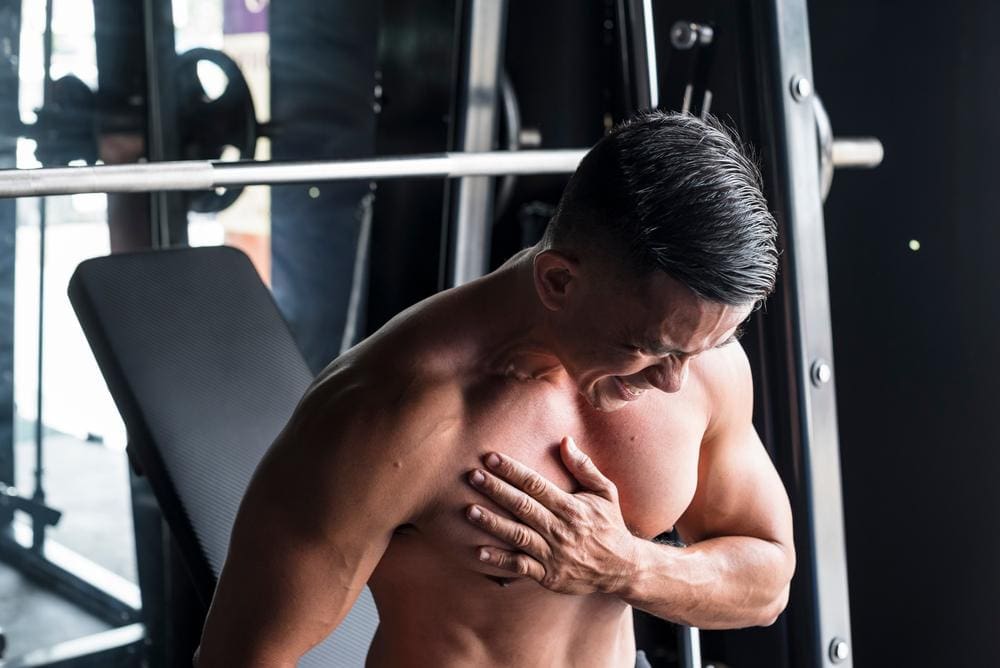 A man at the gym is wincing and grasping his chest because he tore a muscle. 