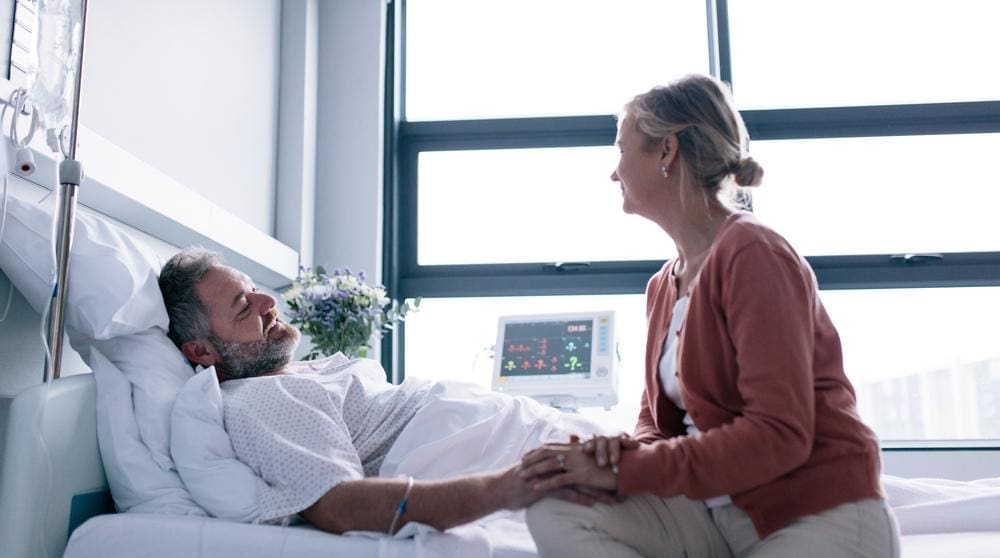 A woman is visiting her husband in the hospital after he had surgery. 