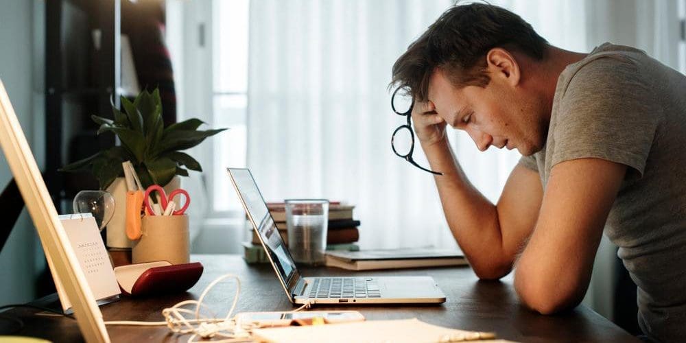 A man is sitting at his desk, looking extremely stressed.