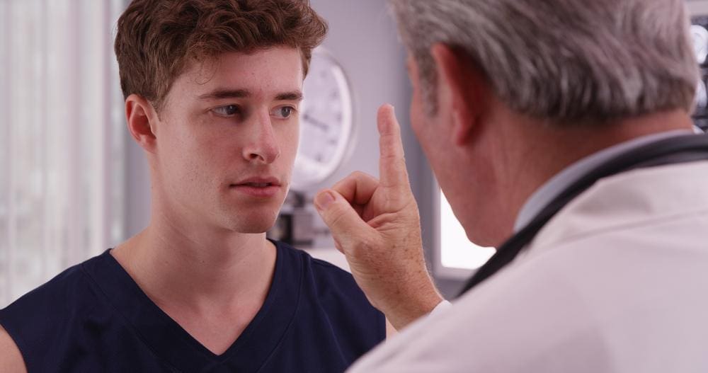 A chiropractor is examining a young man for concussion symptoms.