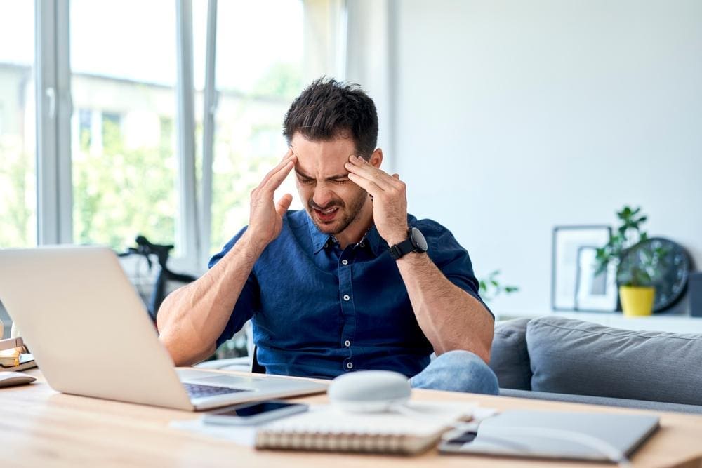 A man is sitting at his desk, unable to work because he is suffering from bad headaches. 