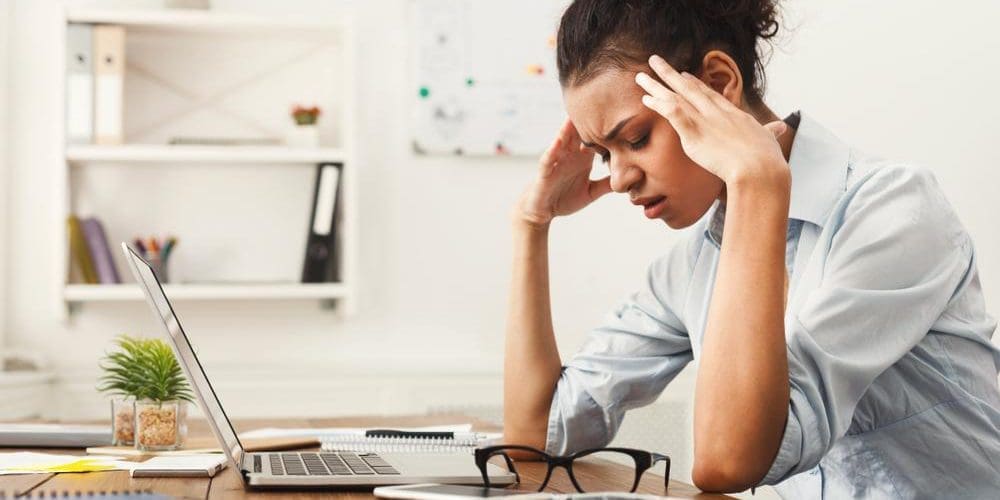 A woman is sitting at her desk suffering from headaches.