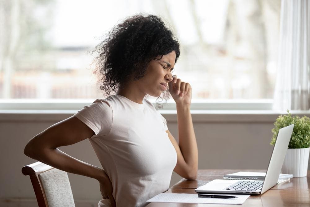 A woman is experiencing pain from tight muscles while sitting at her work desk.