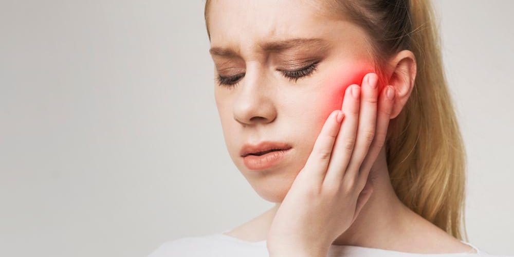 A young woman suffering from trigeminal nerve pain is clutching face.