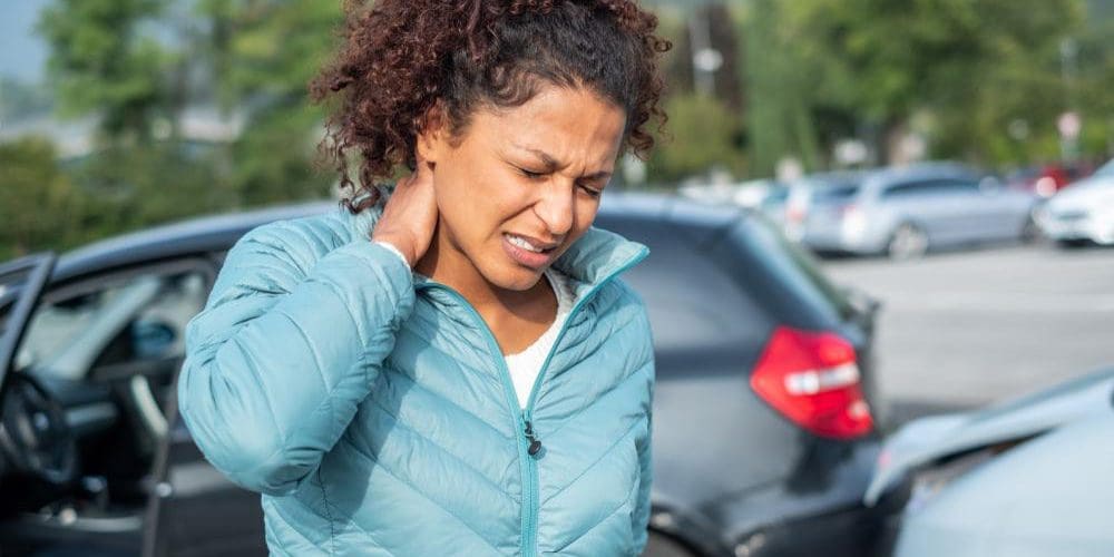 A young woman is holding the back of her neck because she was just in a car accident.