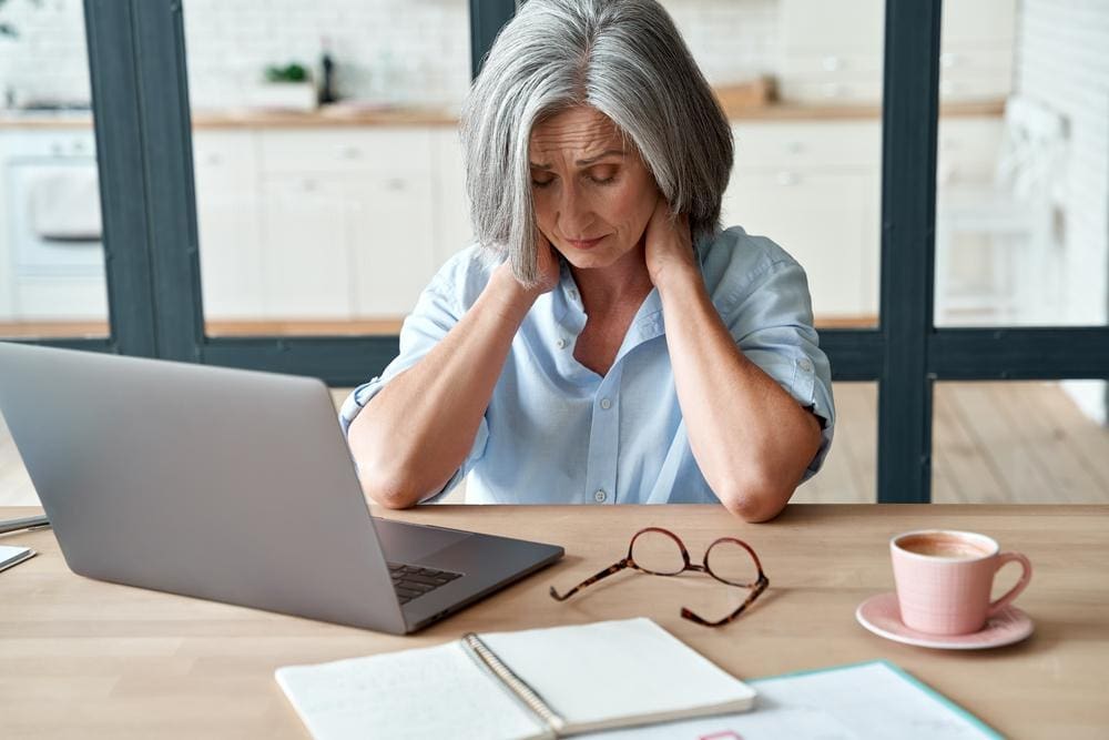 A woman is holding the back of her neck because she is in pain from cervical arthritis. 
