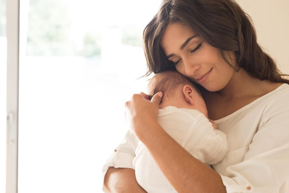 A new mother is cuddles her baby. 