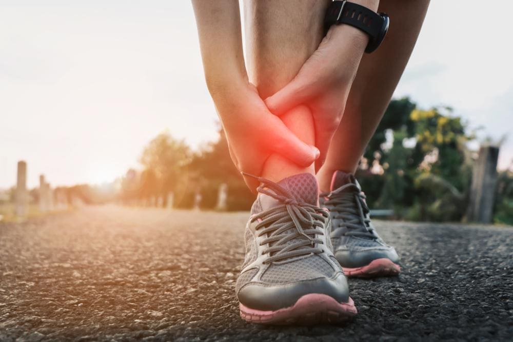 A runner has stopped running and is holding his ankle because he sprained it. 