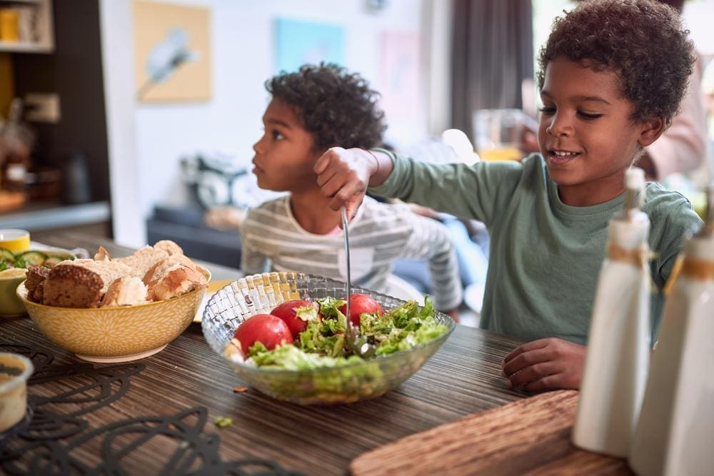 Two young boys sitting at the dinner table eating a healthy meal.