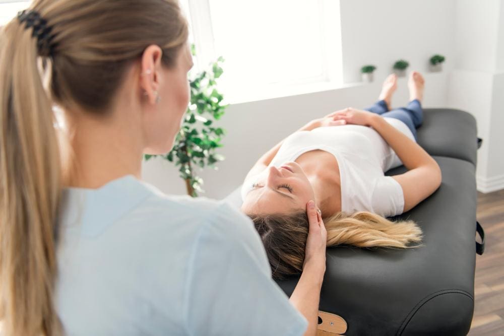 A chiropractor is administering manual adjustments on a female patient suffering from fibromyalgia.