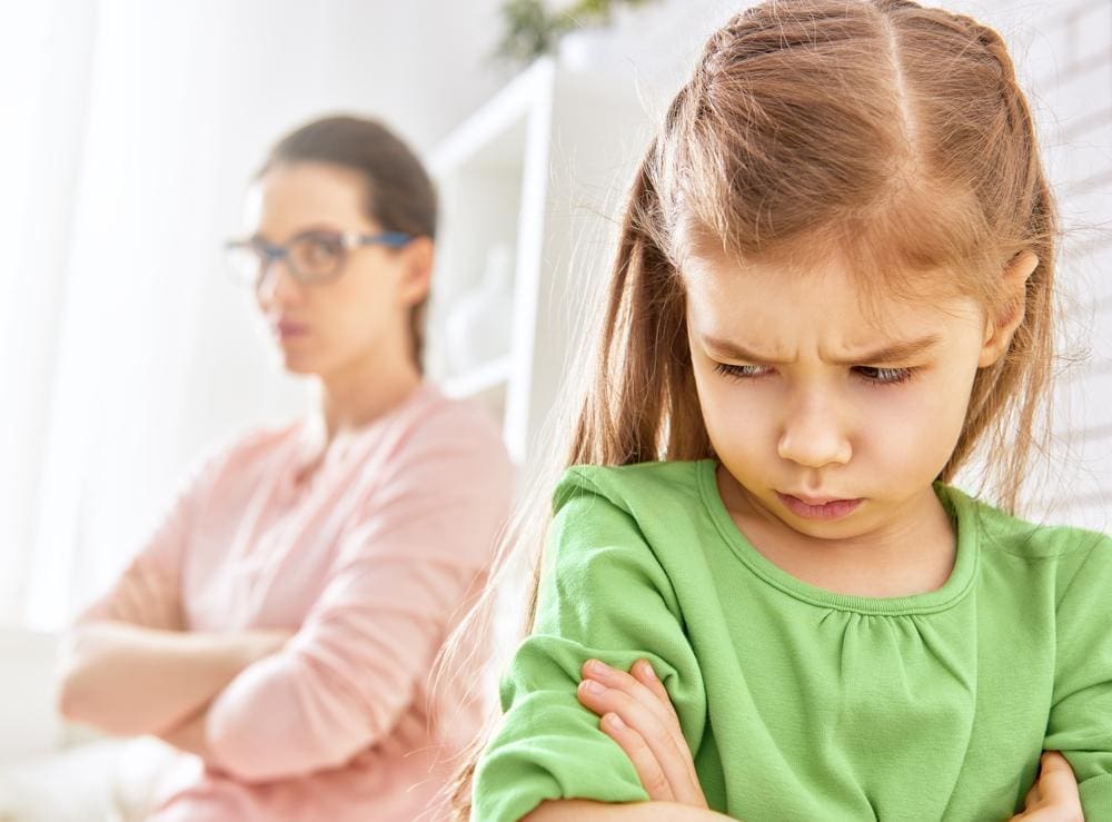A young girl is angry with her arms crossed and will not speak to her mother.