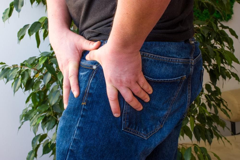 Man experiencing hip pain and holding onto hip with both hands.

