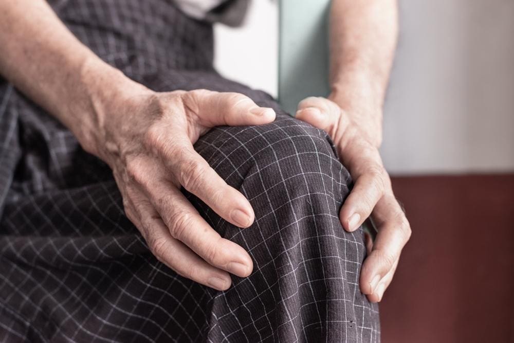 Senior man sitting down and grasping his knee in pain.
