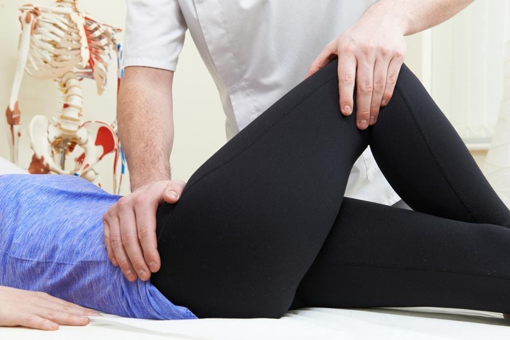 Chiropractor performing manipulation techniques on the hip of female patient.