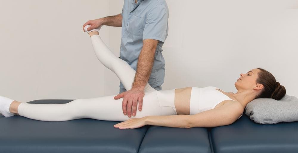 Woman having her hip adjusted by chiropractor while lying on treatment bed.
