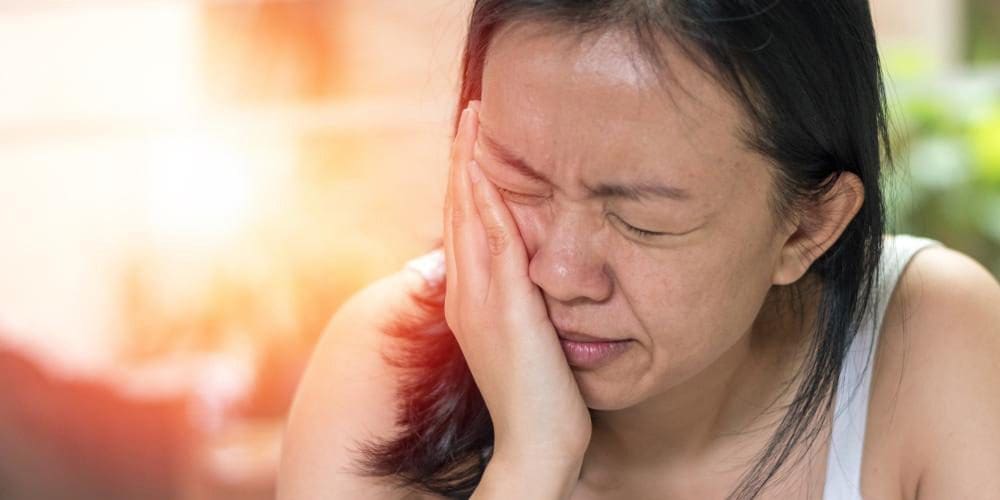 Young woman with Bell’s palsy clutching the side of her face.