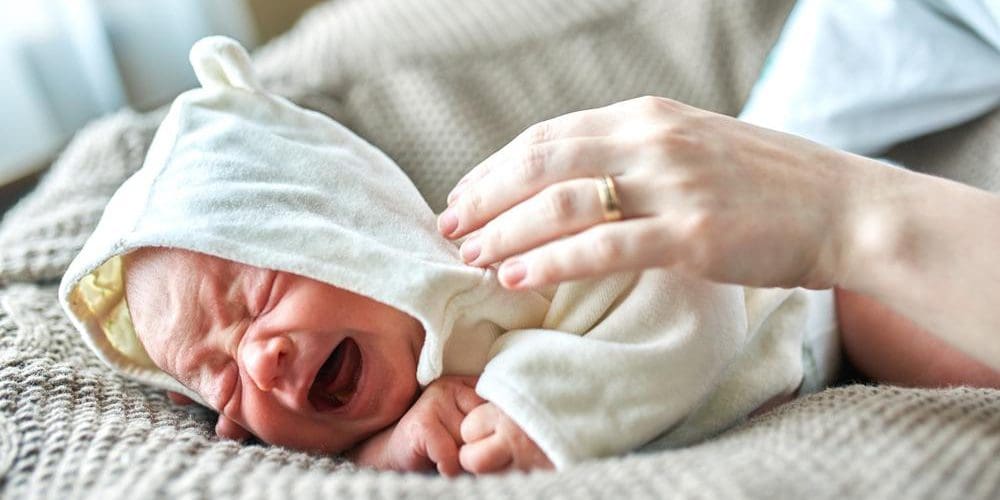 Colicky baby in hooded sweater crying, with the mother trying to console them.