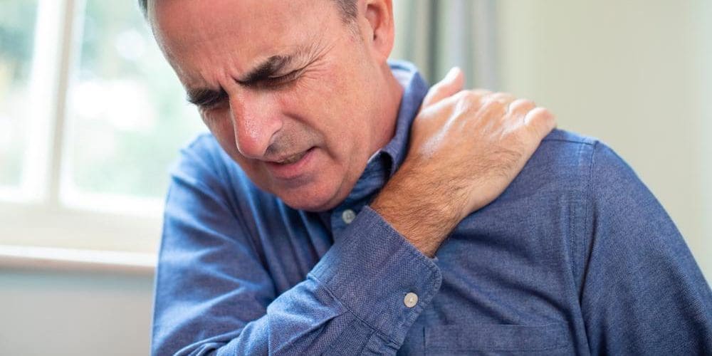 A man is grasping his shoulder, because he suffers from frozen shoulder.